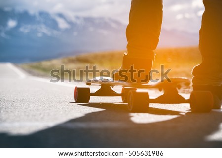 Longboard with athlete's foot is on the road in the mountains. Sunlight.