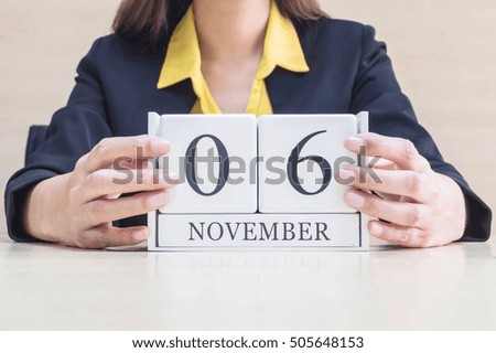 Closeup white wooden calendar with black 6 november word in blurred working woman hand on wood desk in office room , selective focus at the calendar