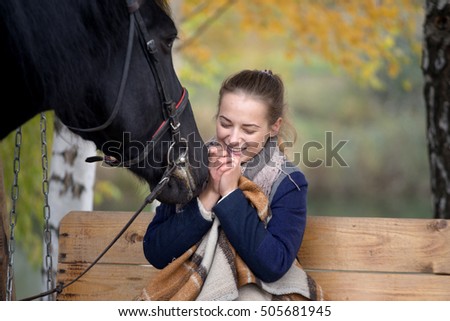 girl in a plaid with a black horse in the autumn under a birch tree on a bench.