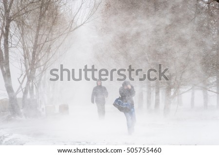 Snowstorm and strong wind in city Nothing visible Silhouettes of two men Blurred image Royalty-Free Stock Photo #505755460