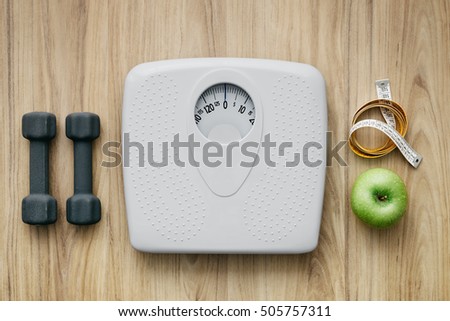 Weight scale, healthy snack, measuring tape and dumbbells on a table, weight loss and sports concept, flat lay Royalty-Free Stock Photo #505757311