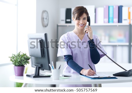 Young practitioner doctor working at the clinic reception desk, she is answering phone calls and scheduling appointments Royalty-Free Stock Photo #505757569