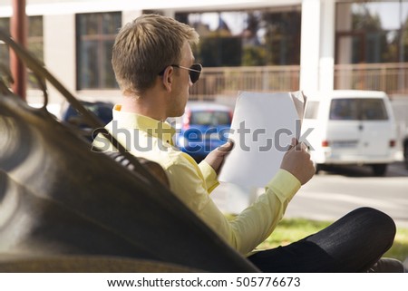 Mock-up newspaper. Man with the newspaper in his hands. Young man reading a newspaper on a bench. Warm autumn day.