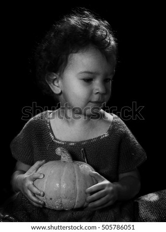 Pretty toddler girl holding a pumpkin with black background. Halloween. Black and white vintage stile picture