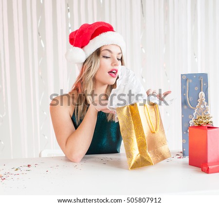 Pretty woman in Christmas hat opening a wrapped gift
