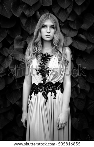 Beautiful girl in silk dress posing by wall covered with ivy, black and white photo