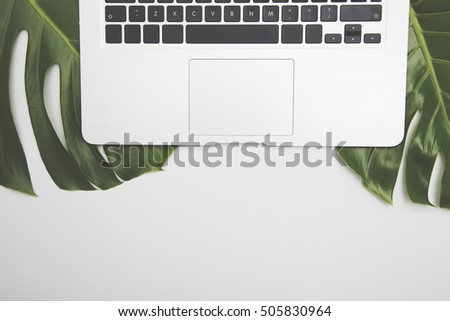 Overhead desk with laptop computer and green tropical leaves