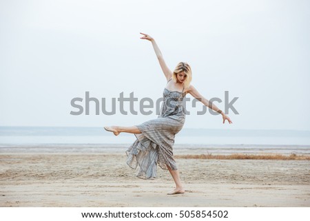 Beautiful young woman dancer in long dress dancing barefoot on the beach