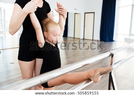 Beautiful little balerina stretching with help of her teacher in ballet studio