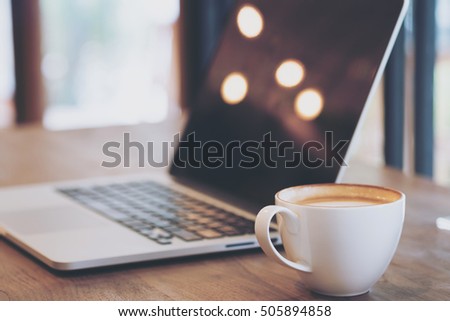 Drink & technology image of hot latte art coffee with laptop on wood table in cafe with light , bokeh flare and abstract 