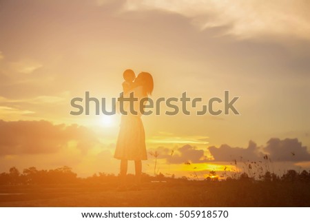 Ha silhouette of a happy young girl child the arms of his loving mother for a hug, in front of the sunset in the sky on a summer day.