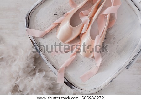 Pastel pink ballet shoes background. New pointe shoes with satin ribbon lay on white rustic shubby chic chair near feather boa, top view from above