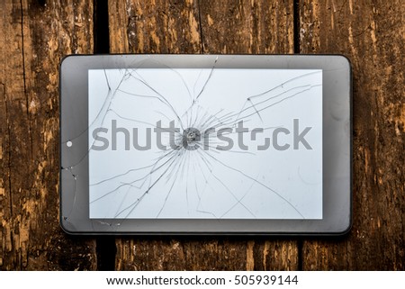Tablet on the wooden table with broken glass