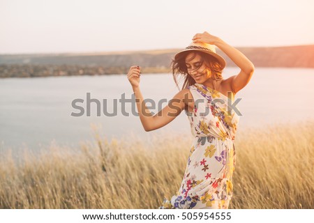 Beauty young girl outdoors enjoying nature. Fashion young woman in floral dress and stylish hat in meadow with copy space Royalty-Free Stock Photo #505954555