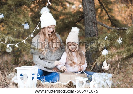 Cute stylish girls wearing knitted hats and sweaters open Christmas presents under Cristmas tree outdoors. Holiday season.