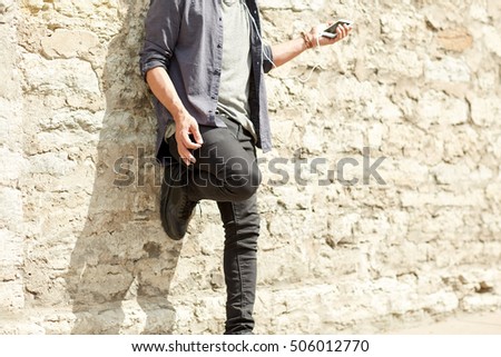 people and technology concept - close up of man with earphones and smartphone listening to music and playing imaginary guitar at brick wall on street