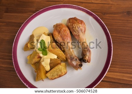 Roasted chicken drumsticks served on the old vintage porcelain plate with baked sweet potatoes and french mustard sauce. Picture isolated on the wooden table closeup. Fresh and health family lunch.