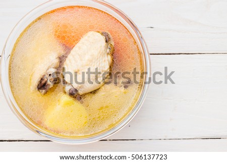 Bowl of chicken soup and chicken wings with carrots, potatoes and tomatoes on wood table 