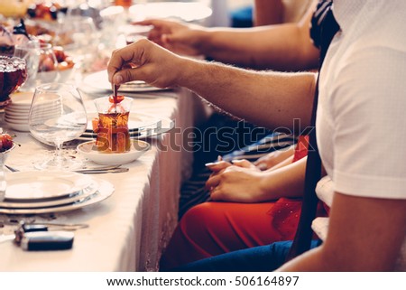 Table setting of traditional tea in eastern glass with red ribbons on the white tablecloth, people mixing sugar in the tea, Arabic, Turkish, Azerbaijani customs, vintage
