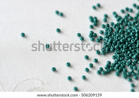 Scattered seed beads of emerald color on the textile background
