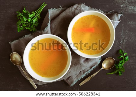 Bouillon or broth served in two bowls on a rustic dark table, view from above