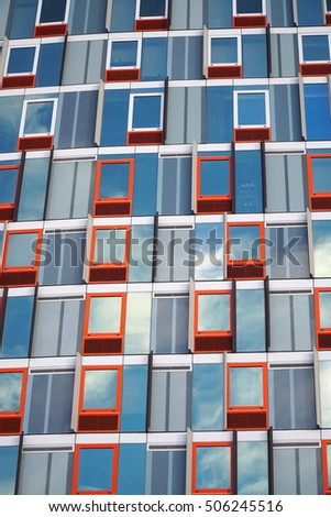 Red outline window pattern with reflecting windows of a cloudy blue sky exterior urban apartment building. Expensive real estate. Vertical photo