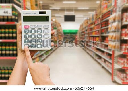 Women hand touching buttons of calculator on the Abstract blurred photo of store in department store background /image for holiday weekend.