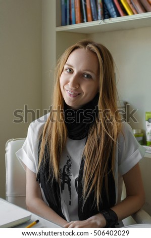 Soft focus photo of pretty young girl behind the table with bookshelf on background. (Image contains a little noise)