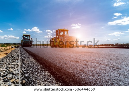 Sunset above the road roller working on the new road construction site Royalty-Free Stock Photo #506444659