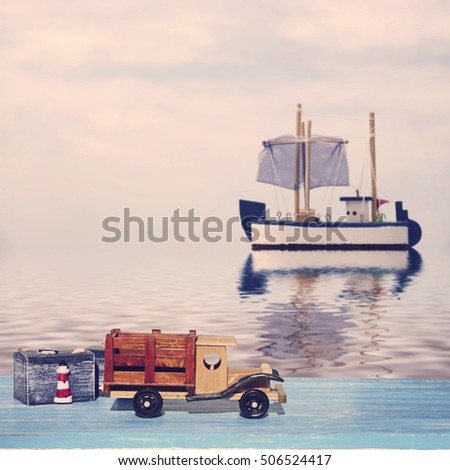 A toy truck car and two chests on a blue wooden surface and a toy sailboat at sea. Photo toned in vintage style