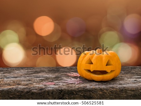 Halloween pumpkin orange Jack O'Lantern happy smiling face on grunge wood table with red autumn leaves, candle light lit bokeh for halloween party holiday celebration decoration