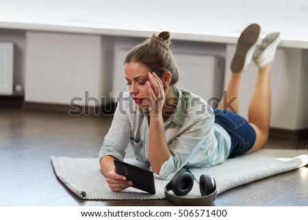 Pretty young hipster woman reading an e-book at home