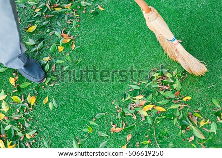 Working with broom sweeps lawn from fallen leaves Royalty-Free Stock Photo #506619250