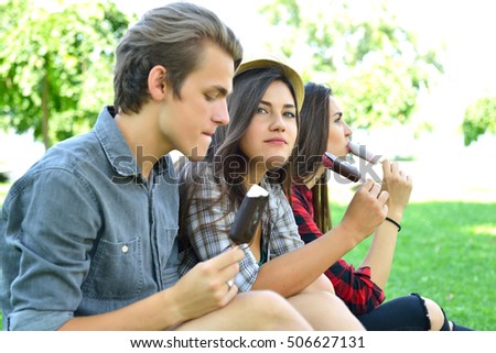 Young man and women eating chocolate ice-cream outdoor in summer park. Friends have fun outdoor. Leisure, youth, summertime.