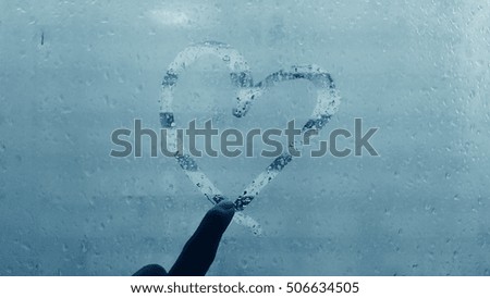 heart by forefinger on glass with raindrop