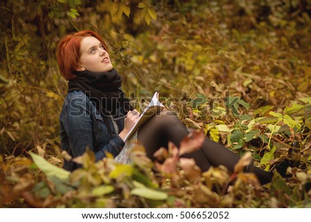 Young Beautiful Redhead Girl Writing To Her Notebook In A Park