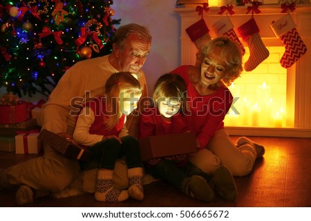 Elderly couple with their granddaughters opening Christmas present near fireplace