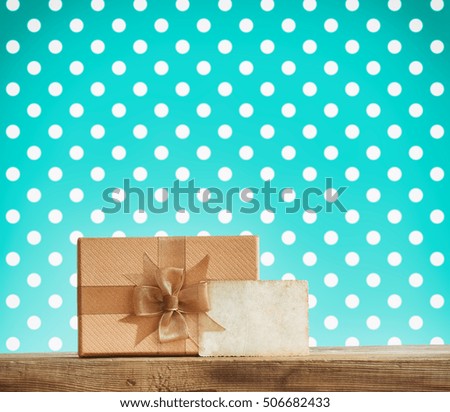 holiday brown gift box with a bow, paper label on a wooden table, turquoise background with polka dots