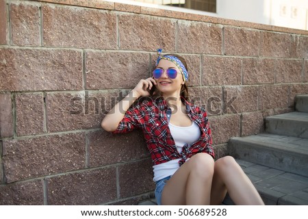 Modern fashion girl is sitting on stairs and talking on the phone