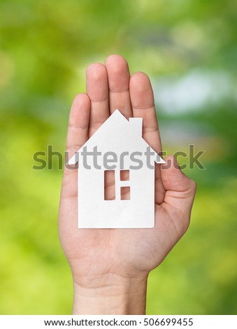 Hand holding white paper house figure on green background. Real Estate Concept.