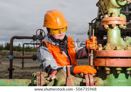 Woman engineer in the oilfield repairing wellhead with the wrench wearing orange helmet and work clothes. Oil and gas concept. 