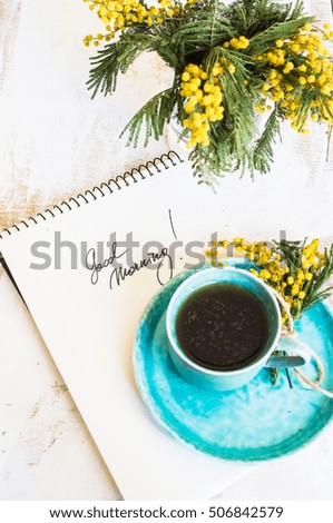 Cup of coffee with yellow mimosa flowers and good morning note on rustic wooden table