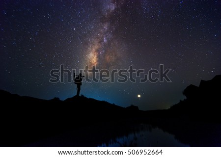 Milky Way has stars and the night sky with the silhouette of a backpack. Carrying a camera and a tripod standing on the hill.