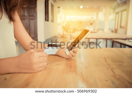 Online payment,Woman's hands holding a credit card and using smart phone for online shopping in coffee shop with morning light. Vintage filter effect.