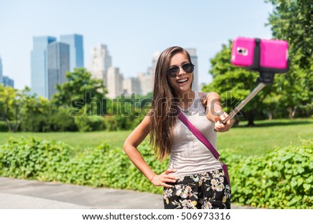 Happy travel tourist taking self-portrait picture with mobile phone and selfie stick at popular attraction in NYC. Central park woman walking in summer park in New York City, Manhattan, USA.