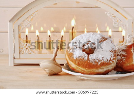 Selective focus image of jewish holiday Hanukkah with menorah (traditional Candelabra), donuts and wooden dreidel (spinning top)