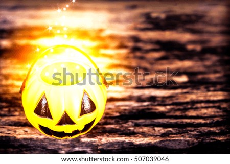 Dark tone photo with of Halloween pumpkin face with warm golden dot evaporate on top of bucket over old wooden texture