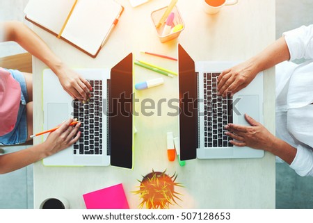 Top view of two coworkers people working on a laptop computer at the desktop. Colleagues or business professionals keyboarding text on net-books at office table. Freelancers at creative project 