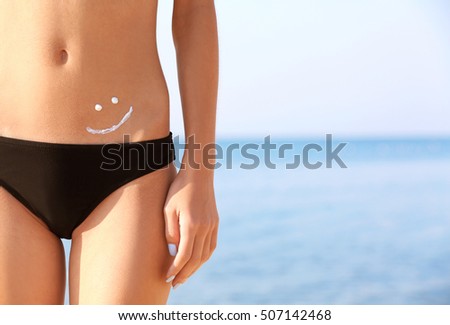 Young woman with sunscreen on body, sea background