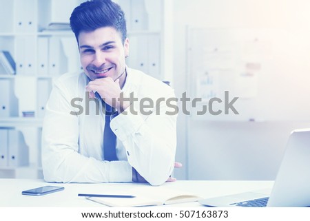 Young businessman in white shirt sitting at his office desk smiling to camera. Concept of corporate business and happiness. Toned image